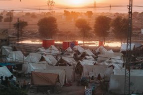 I soluppgången syns ett tältläger med vita tält som står tajt tillsammans. I bakgrunden syns vattnet som har översvämmat stora delar av Pakistan.