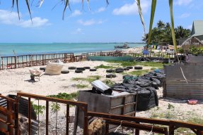 Längs en vit sandstrand ligger bilddäck utspridda och stora svarta sopsäckar står uppradade som en skyddsmur. 