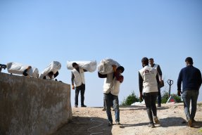 Flera män i Läkare Utan Gränser västar bär påsar med tält över sina axlar.