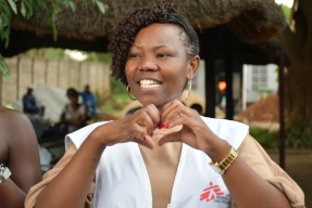 En ung kvinna med MSF-väst gör ett hjärta med händerna