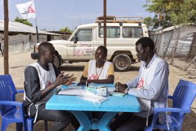 Tre personer i Läkare Utan Gränser västar sitter runt ett bord och diskuterar.