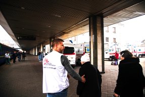 En man i Läkare Utan Gränser väst leder två kvinnor mot ett tåg