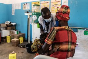 En läkare står framför en kvinna som håller ett banr i famnen. 