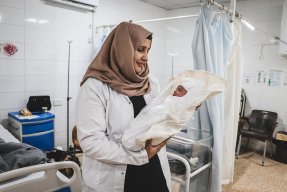 en barnmorska håller en nyfödd bebis insvept i vitt tyg på en mödravårdsavdelning