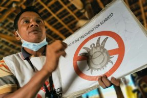 en anställd på Läkare Utan Gränser håller upp en skylt med en bild på parasiten som orsakar skabb