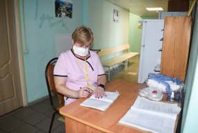 Kvinna i rosa t-shirt sitter vid skrivbord och antecknar i block.