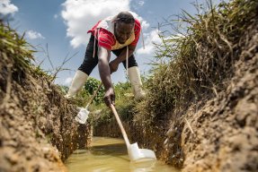 En man skyfflar upp vatten ur en damm.