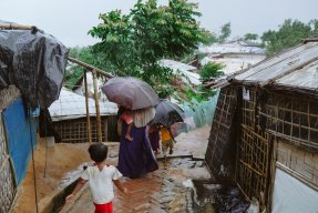 En familj går längs en gata, på båda sidor syns skjul bygda av bambu och plastskivor.