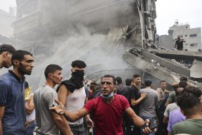 en samling människor vid en sönderbombad byggnad i Gaza