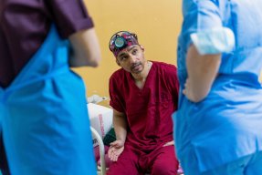 en man i operationskläder och en pannlampa diskuterar med kollegor på ett sjukhus i Khartoum