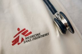 Närbild på Läkare Utan Gränsers logotyp tryckt på vitt tyg, till höger hänger ett stetoskop.