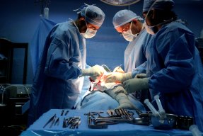 Tre kirurger utför en operation på en patients ben.