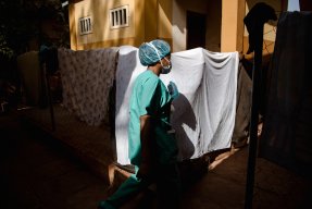 Kvinna iklädd sjukvårdskläder går framför lakan som hänger på tvättlina.