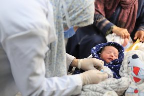 Ett nyfött barn i en filt får vård av en sjuksköterska.