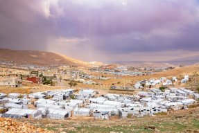 Vy över Arsal, vita hus, berg och färgglad himmel.