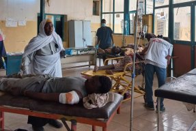 På sängar i ett rum ligger patienter omgivna av personal.