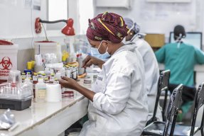 En kvinna i labbkläder och munskydd analyserar bakterieprov i ett laboratorium