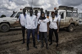 Personal från Läkare Utan Gränser tittar mot kameran framför en MSF-bil.