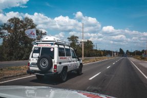 En ambulans med en flagga med Läkare Utan Gränsers logga på en rak asfalterad väg. 