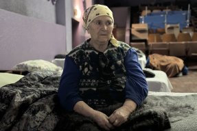 en äldre kvinnar sitter på en tältsäng i en stor sal