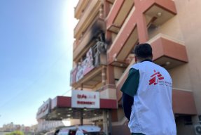 Man i Läkare Utan Gränser-väst utanför en byggnad med spår av angrepp