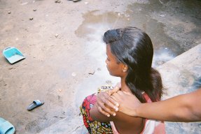 en ung kvinna sitter med ryggen mot kameran och någon lägger sin hand på hennes axel