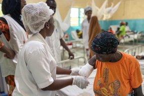 En kvinna i vita sjukhuskläder undersöker en kvinna med en bandagerad arm som slutar vid armbågen.