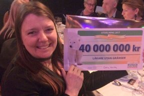 En kvinna håller upp en jättestor check från Postkodlotteriet