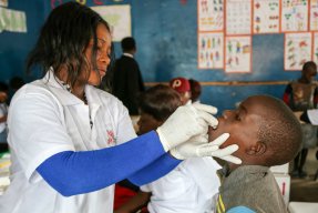 En kvinnlig vårdanställd med skyddshandskar ger ett barn ett oralt vaccin.