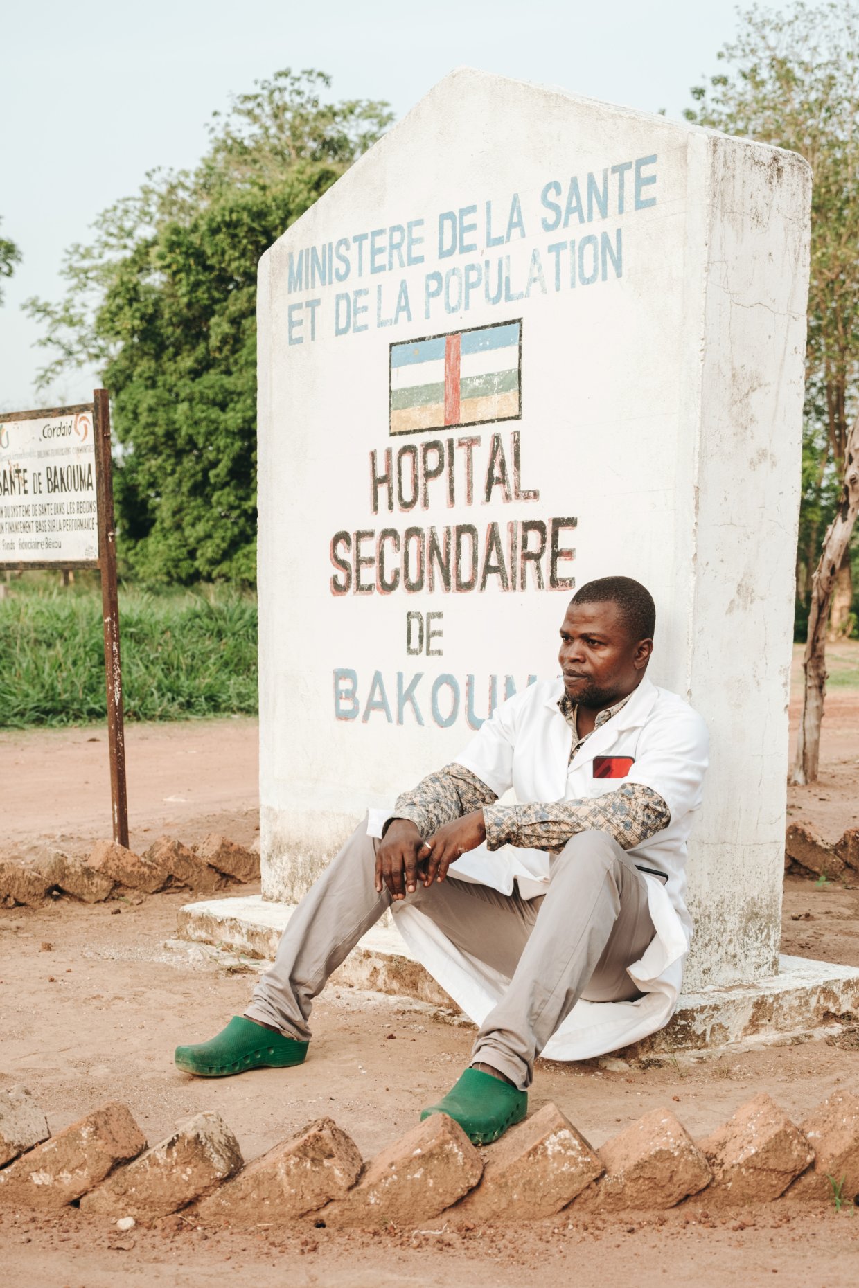 En man sitter på marken vid en sjukhusskylt.