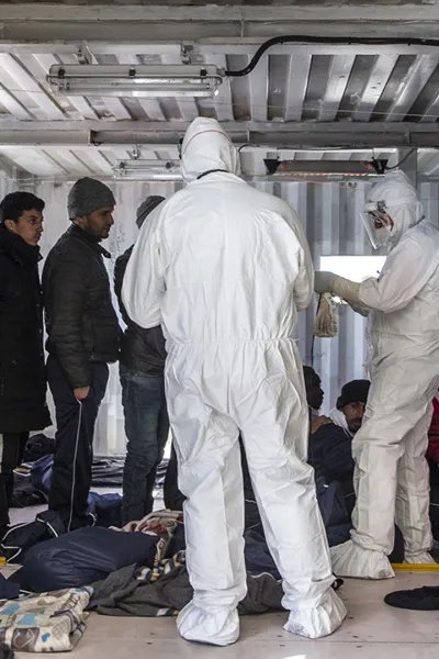 Två personer i skyddsdräkt kontrollerar migranter ombord Ocean Viking
