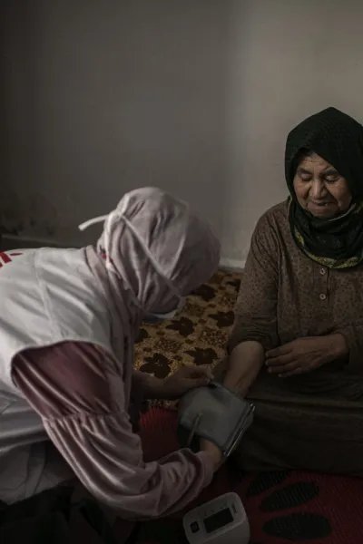 En sjuksköterska mäter blodtrycket på en äldre kvinna som sitter ner.