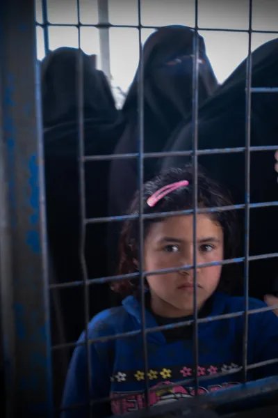 En flicka som bor i lägret Al-Hol i Syrien tittar genom ett stängsel.