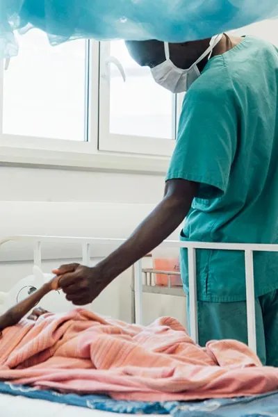 Tvååriga Sheku Kamara, som ligger på sängen på Läkare Utan Gränsers sjukhus i Kenema, Sierra Leone, håller en anställd i handen.