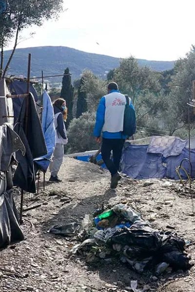 En anställd från Läkare Utan Gränser går, med ryggen mot kameran, på en grusväg genom ett läger på den grekiska ön Samos.