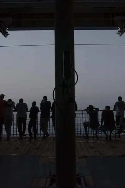 Flera människor står i motljus på däck ombord på sök- och räddningsfartyget Geo Barents och tittar ut mot havet.