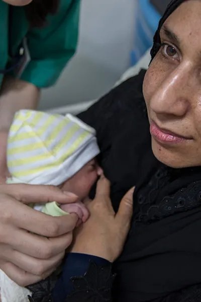 En nybliven mamma på Rafik Hariri sjukhus i Beirut, Libanon, har sitt barn tätt intill bröstet, sjukvårdpersonal står lutad över sängen med en hand på barnet.