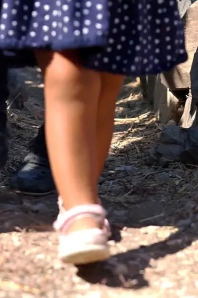 Ett barn i sandaler och klänning går på en grusstig på den grekiska ön Lesbos, endast benen syns.
