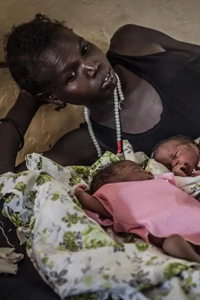 En mamma ligger på en sjukhussäng aå Aweil-sjukhuset i Sydsudan och tittar på sina nyfödda tvillingar som ligger framför henne på sängen.