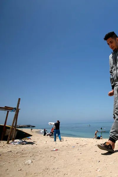 En ung man går på kryckor på en strand i Gaza, Palestina.