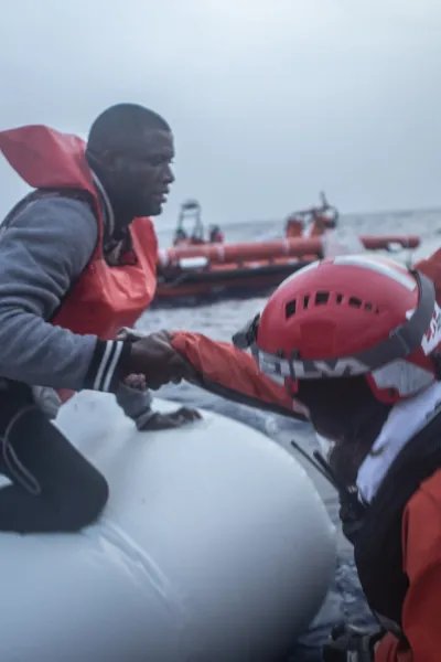 En man får hjälp av Läkare Utan Gränsers medarbetare att ta sig från en vattenfylld gummibåt till vår båt som ingår i vår sök- och räddningsinsats på centrala Medelhavet.