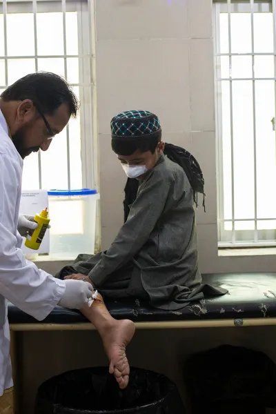 En pojkes sår på benet rengörs av en läkare. Pojken har även bandage på näsan.