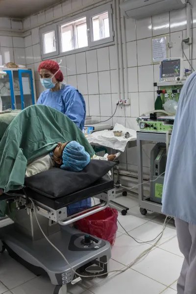 En kvinna ligger på en säng med läkare runt omkring henne