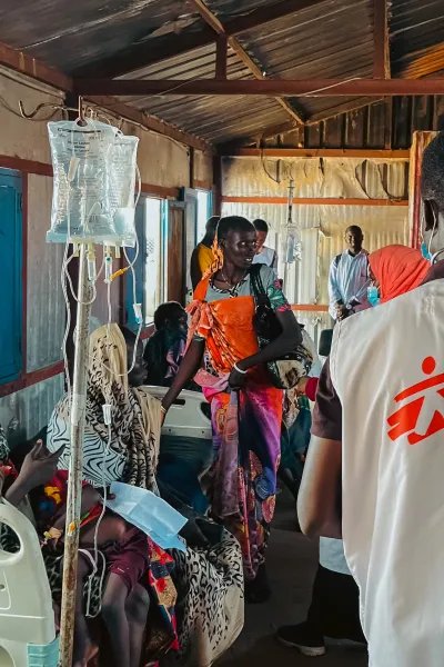Ryggtavla av MSF-anställd omringad av patienter på en klinik.