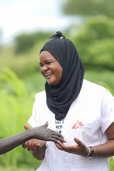 En kvinna i Läkare Utan Gränser väst och slöja skrattar tillsammans med två MSF volontärer.