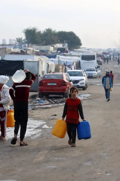 Flera människor bärandes på vattendunkar går längs en gata södra i Gaza.