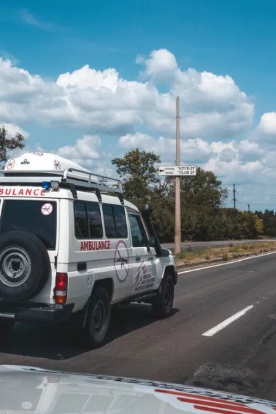 En ambulans med en flagga med Läkare Utan Gränsers logga på en rak asfalterad väg. 