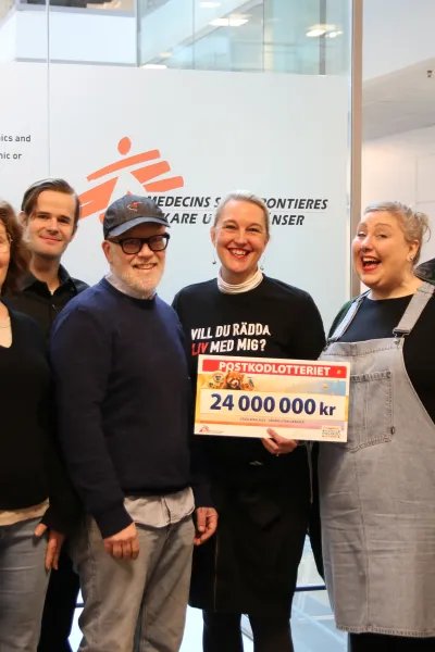 En grupp glada personer håller i en check där det står 24 miljoner