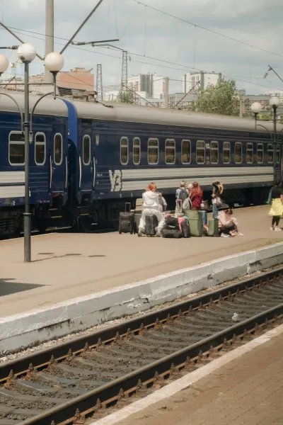 Tågräls och ett tåg med människor som väntar med väskor på perrongen.