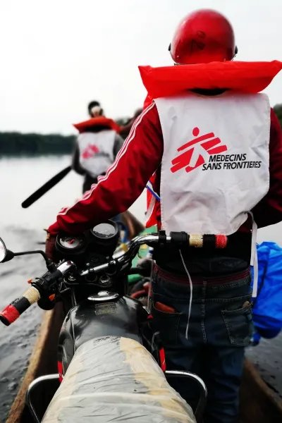 Två personer transporterar motorcyklar i en kanot över floden.